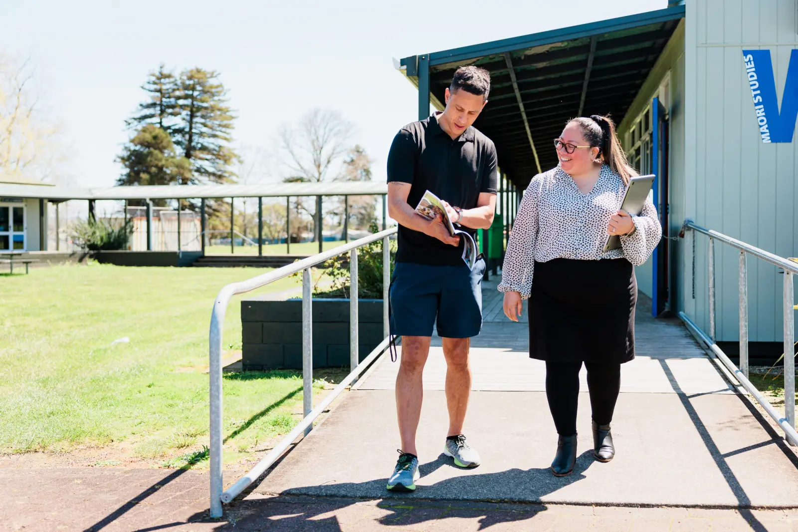 Two teachers looking at a brochure outside a school building